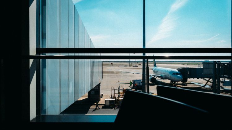 View from airport terminal window showing an airplane docked at the gate under a clear blue sky.